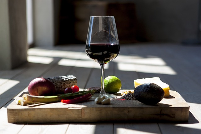 An array of colorful, fresh vegetables alongside a bottle of red wine, arranged on a wooden table with a rustic backdrop.